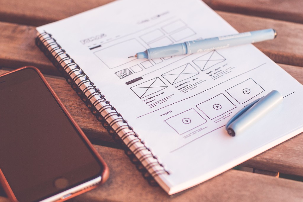 Carnet de wireframes dessinés à la main, stylo et téléphone sur une table en bois